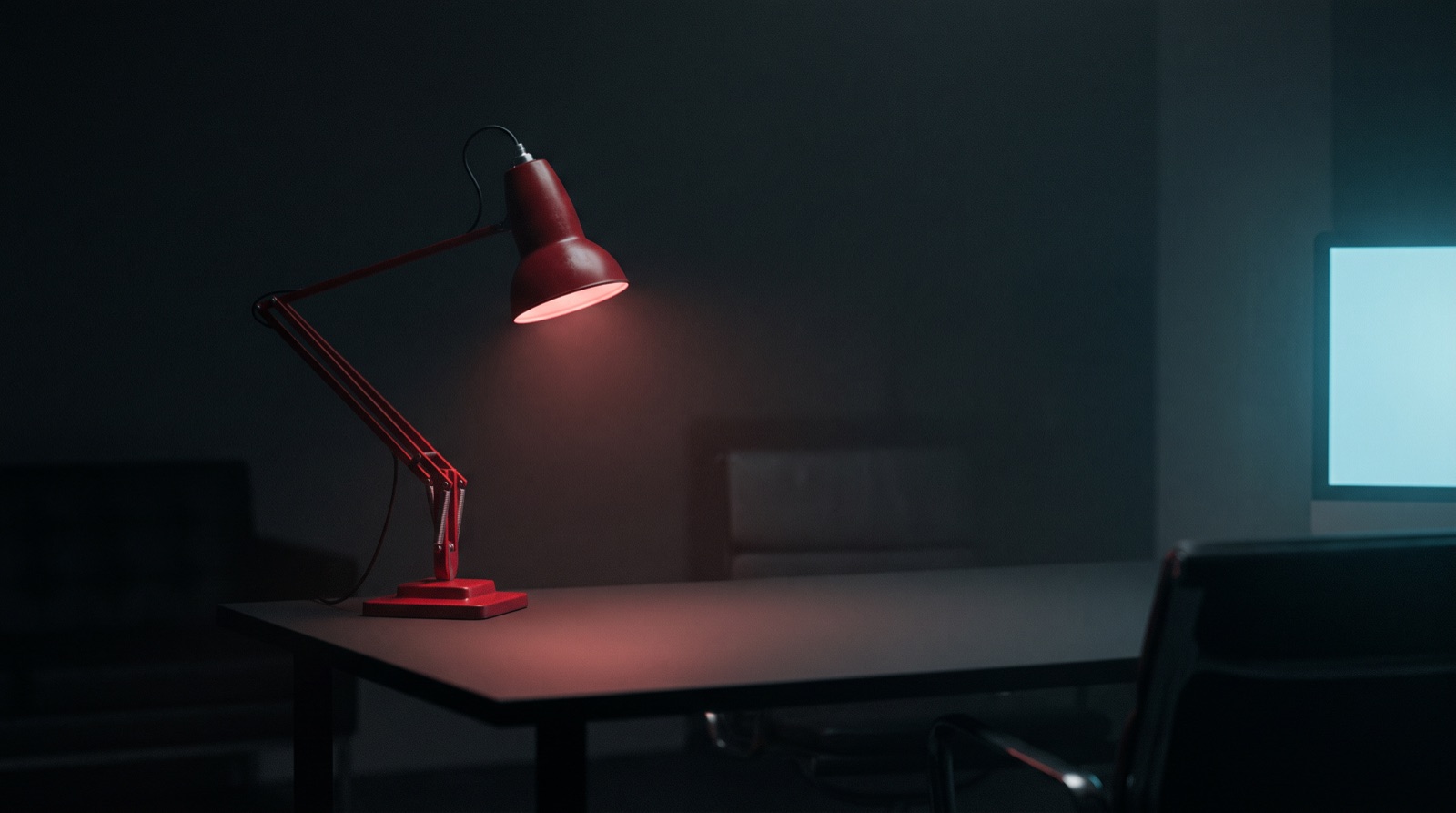 A red desk lamp glowing on a dark desk at night